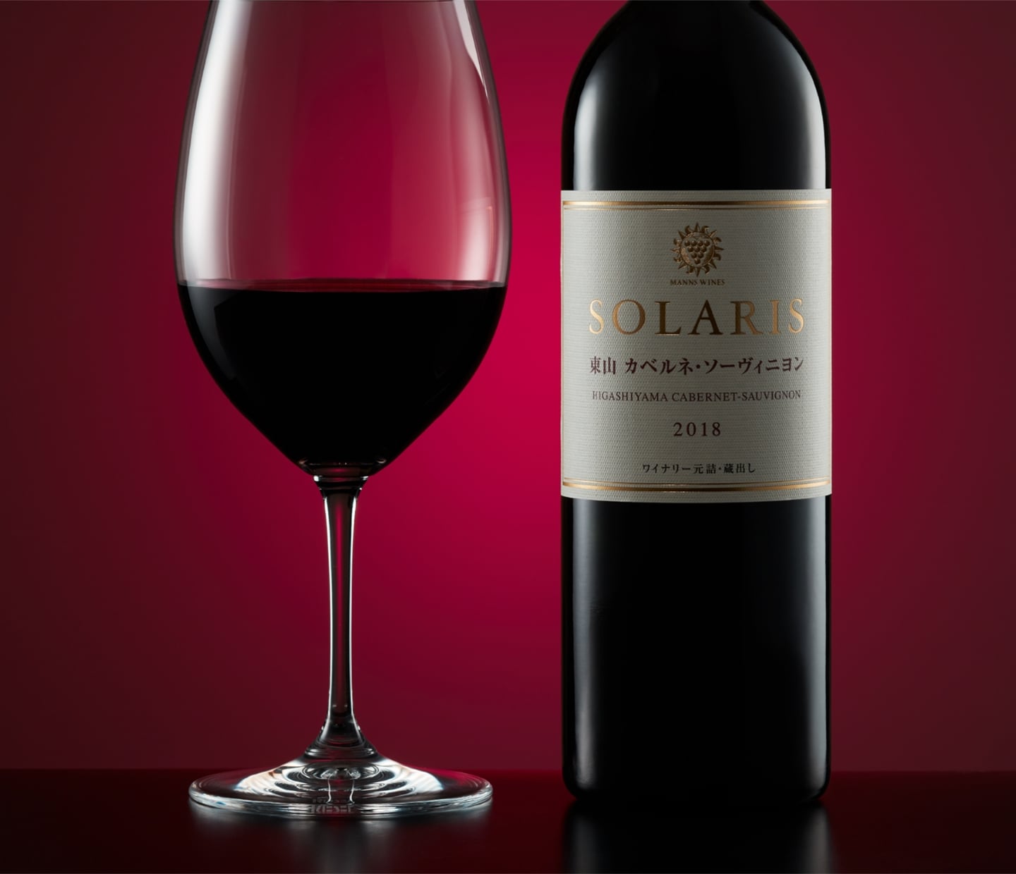 赤い背景の前に、SOLARISの赤ワインボトルと、赤ワインが注がれたワイングラスが並んでいる。ラベルには『SOLARIS 東山 カベルネ・ソーヴィニヨン 2018』と記され、上質で落ち着いた印象の商品カット。